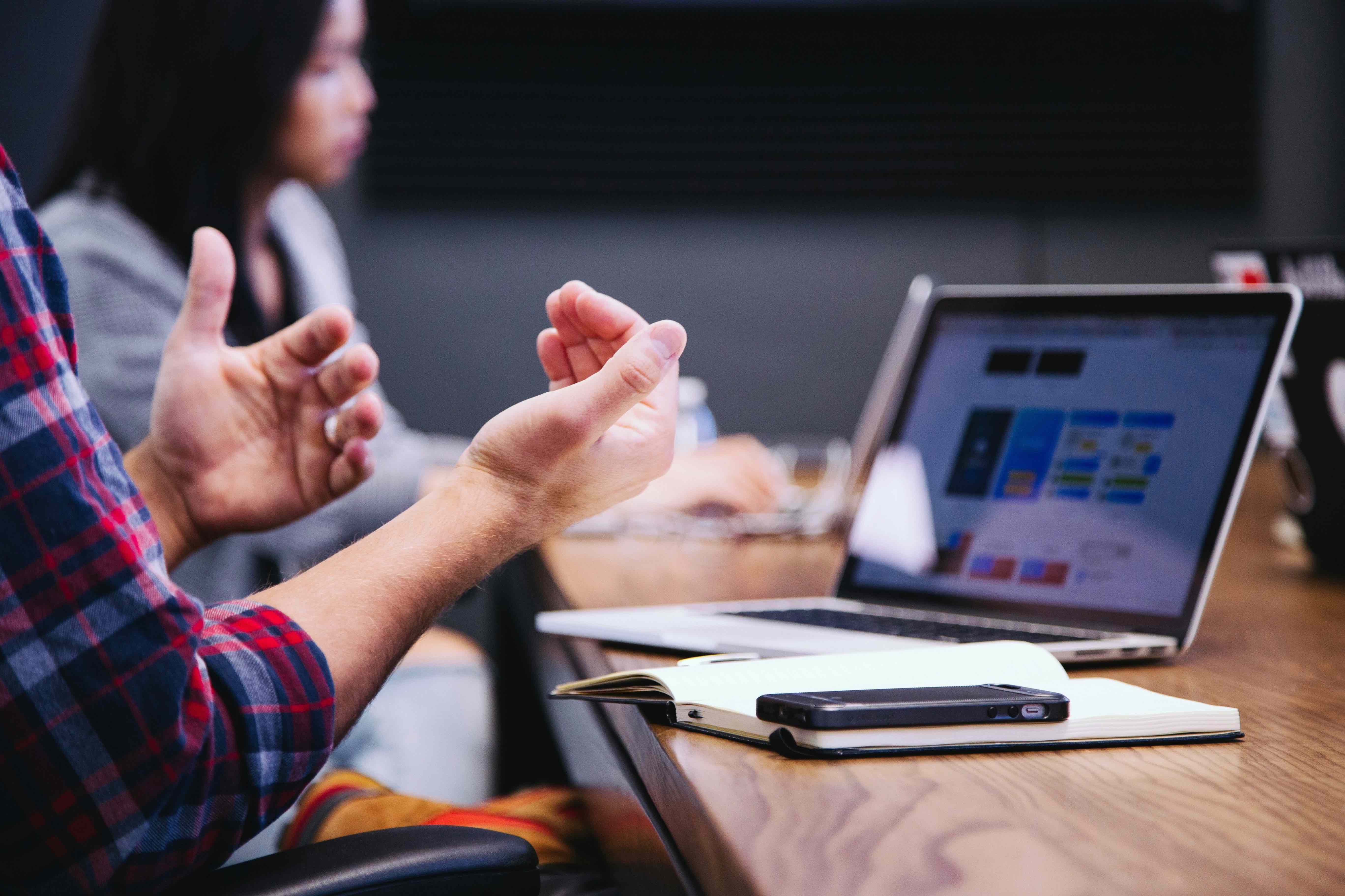 Team members gesturing during a meeting around a table with laptops